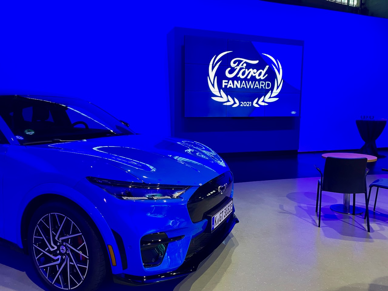 Blauer Ford Mustang Mach-E vor einer Leinwand mit Ford Logo
